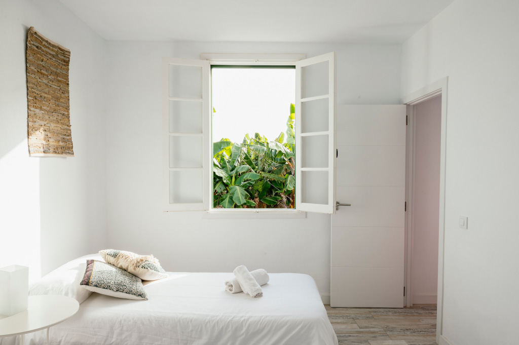 Chambre blanche avec lit, fenêtres ouvertes, vue sur feuillage à Tenerife.