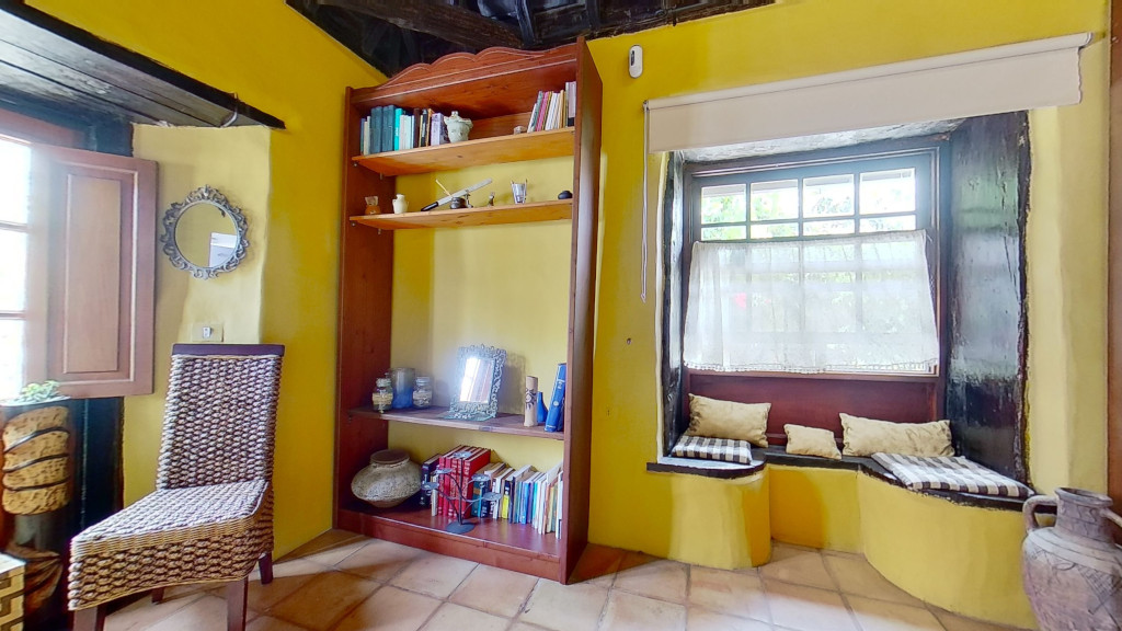 Salle jaune avec chaise en osier, étagères et fenêtre à Icod de los Vinos.