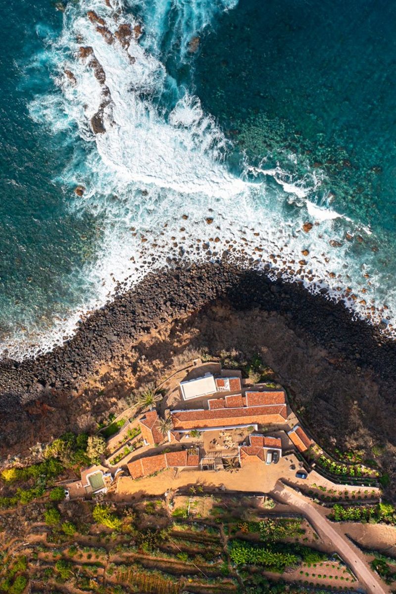 Vue aérienne d'une maison côtière entourée de végétation à Tenerife, bord de mer rocheux.