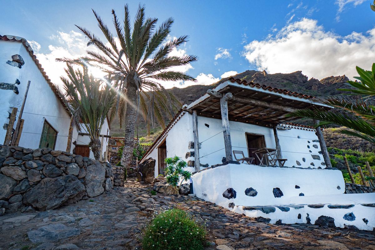 Maison traditionnelle à Tenerife avec palmiers et paysage de montagne en arrière-plan.