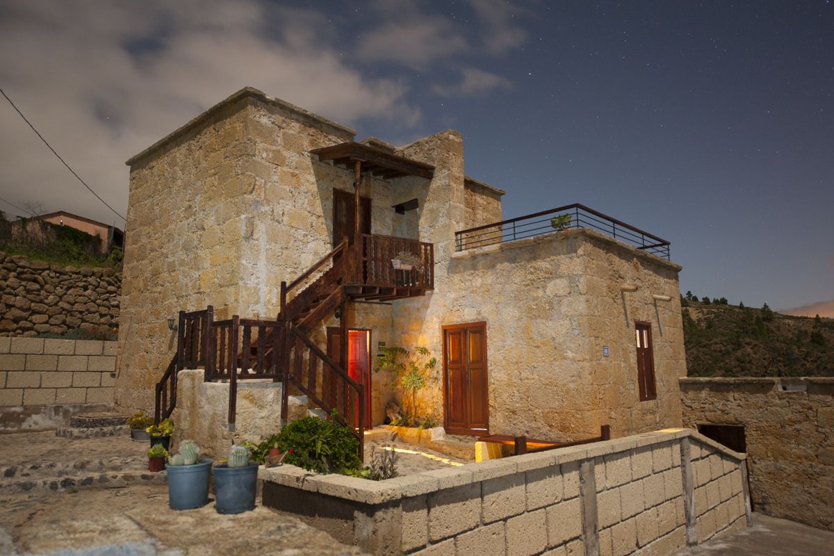 Maison en pierre traditionnelle éclairée la nuit à Tenerife, avec pots de plantes.