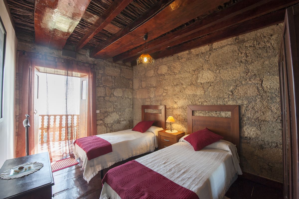 Deux lits simples dans une chambre rustique en pierre avec lampes à Adeje, Tenerife.