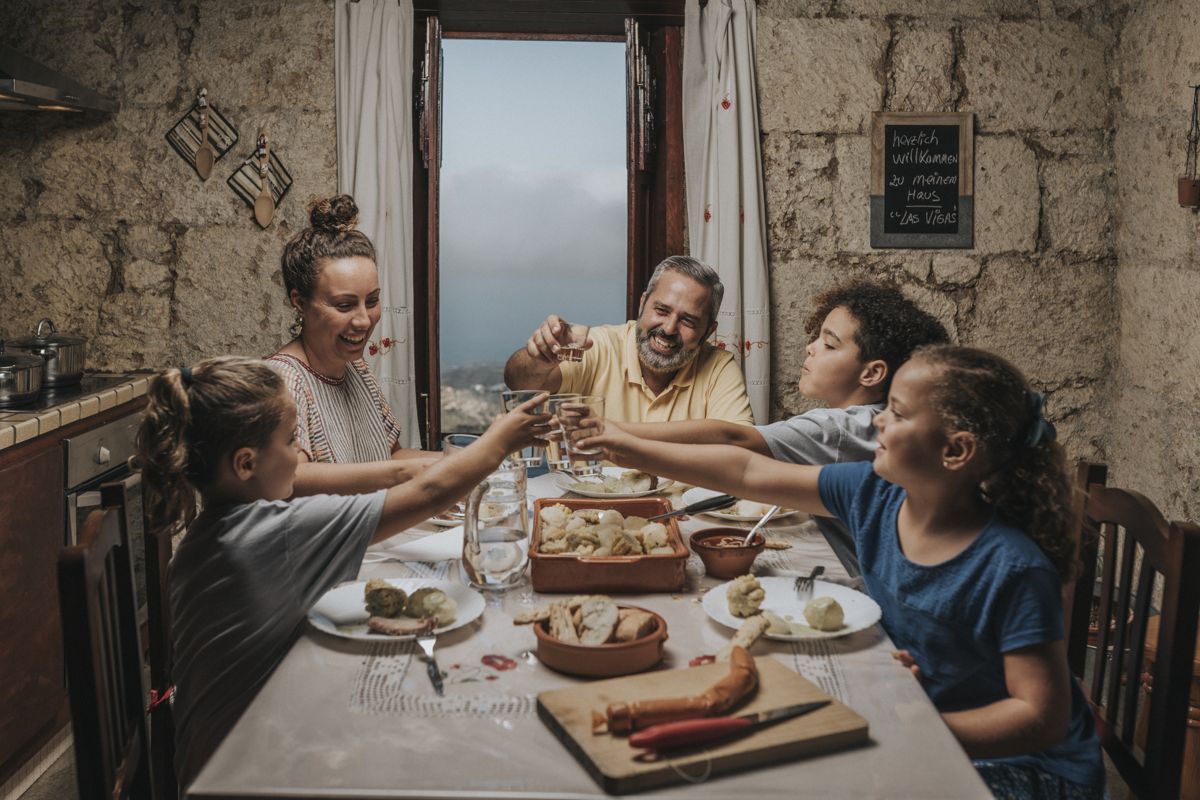 Famille partageant un repas avec vue sur Las Viñas, Tenerife, et texte herzlich willkommen.