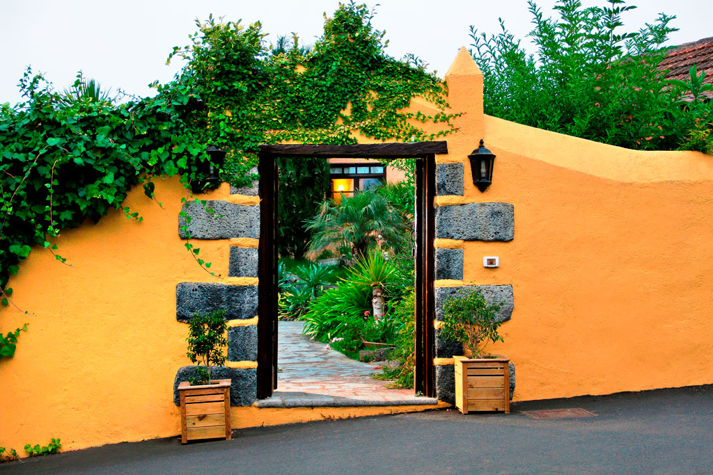 Entrée arborée à La Orotava, passage sous arche jaune vers jardin.