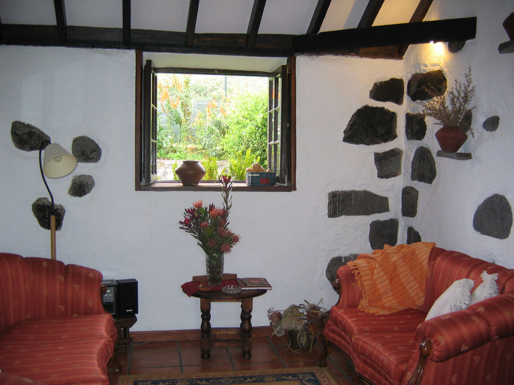 Salon rustique avec canapé rouge, table basse et fenêtre ouverte sur jardin à Tenerife.