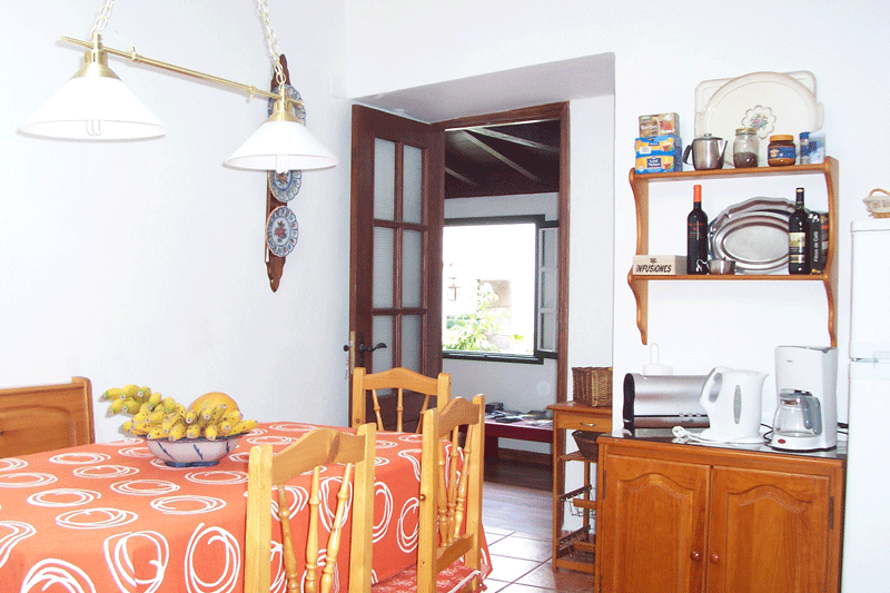 Salle à manger rustique à Tenerife avec table, chaises et étagères de cuisine.