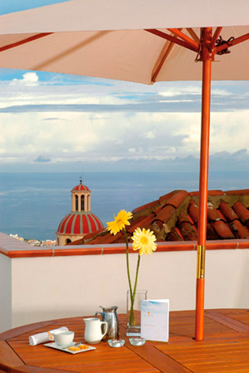 Terrasse avec vue sur océan et clocher à Tenerife, table dressée avec fleurs jaunes.