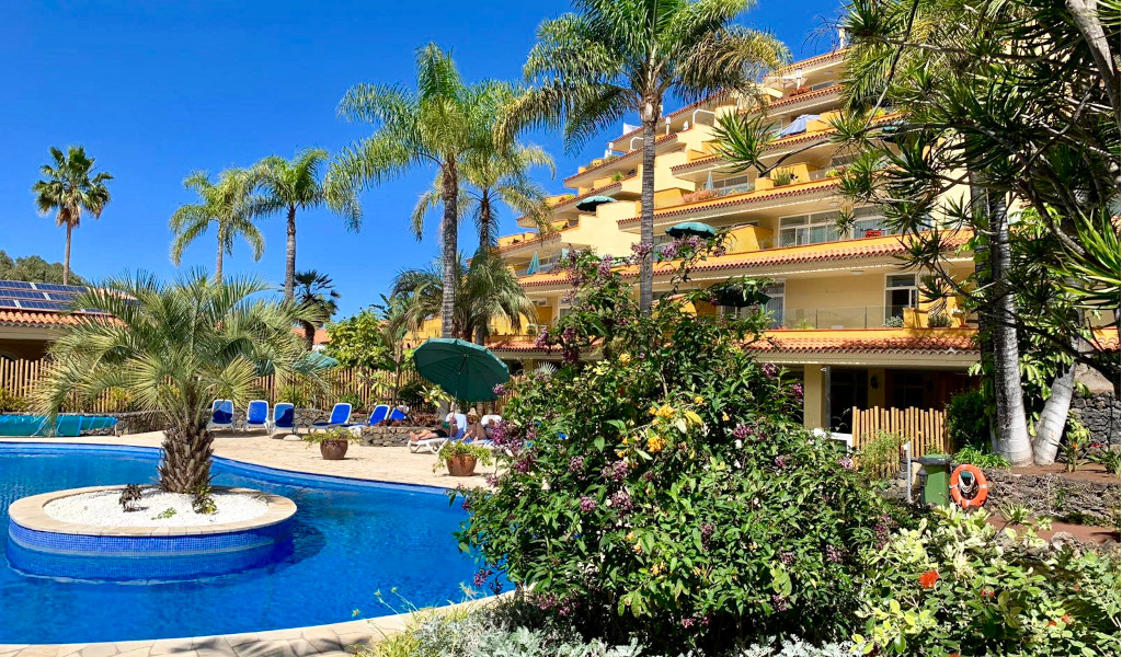 Piscine entourée de palmiers et jardin dans un complexe hôtelier à Tenerife.