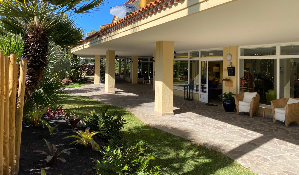 Entrée couverte d’un bâtiment avec jardin à Tenerife, canapés et chaises.