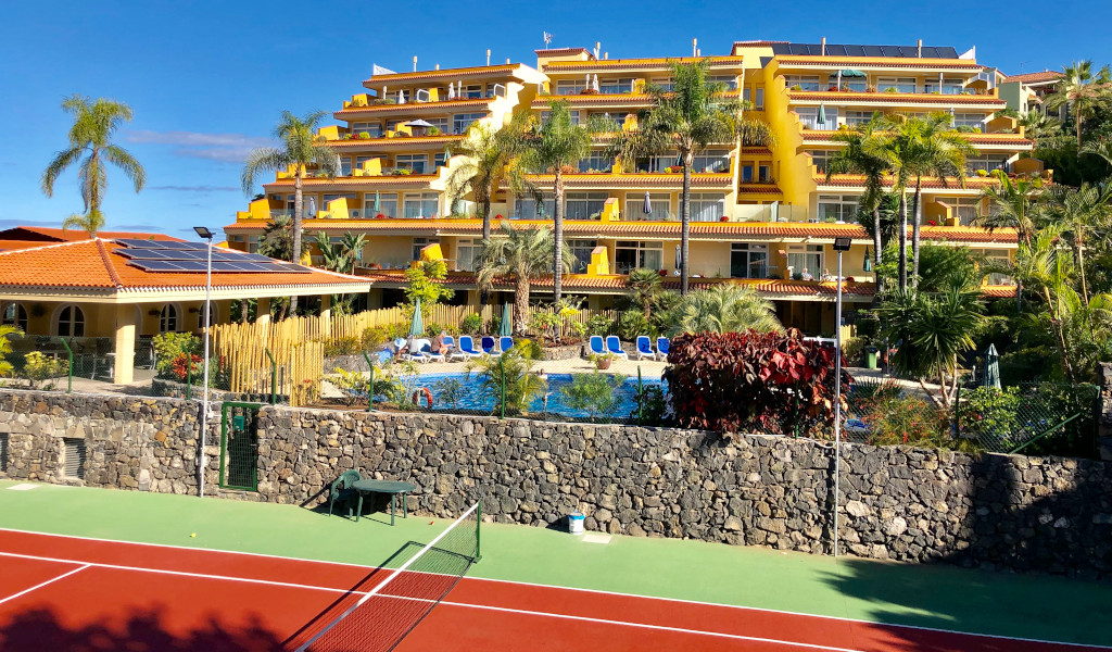 Complexe hôtelier à Tenerife avec piscine, palmiers et terrain de tennis en premier plan.