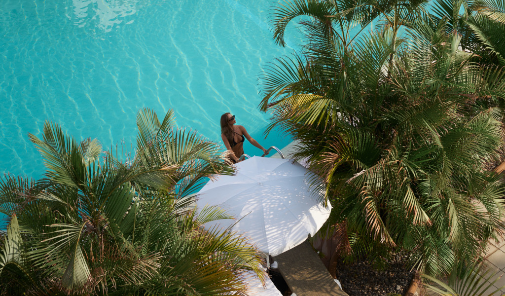 Femme marchant vers une piscine à Tenerife, entourée de palmiers.