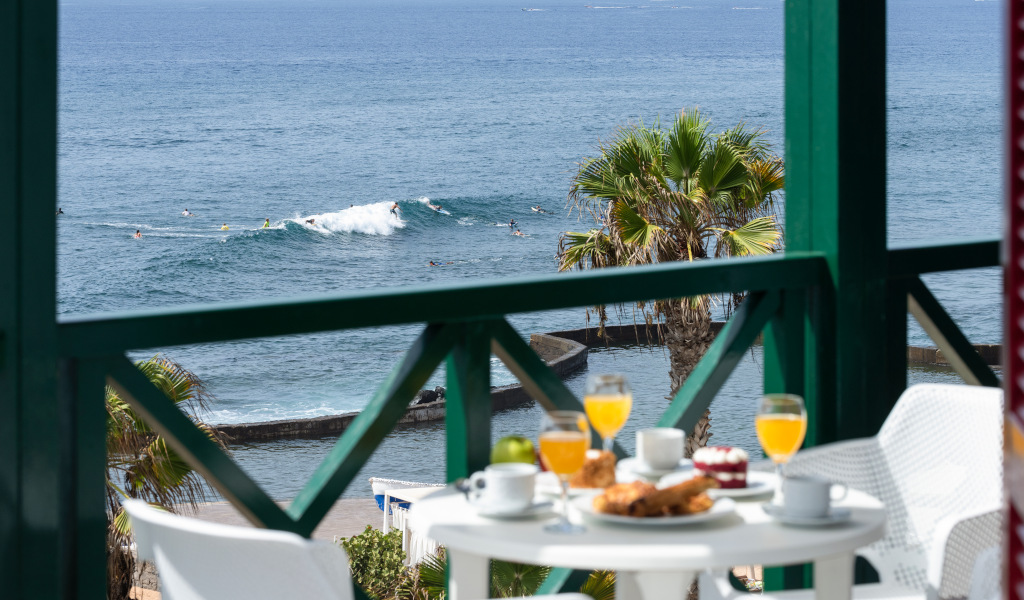 Petit-déjeuner sur terrasse avec vue sur mer et surfeurs à Tenerife.