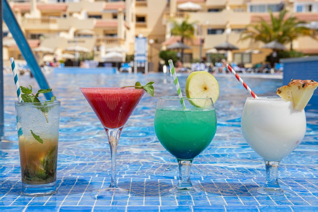 Quatre cocktails colorés alignés devant une piscine à Tenerife.