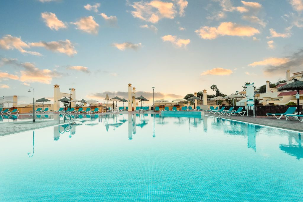 Piscine avec chaises longues et parasols à Tenerife au coucher du soleil.
