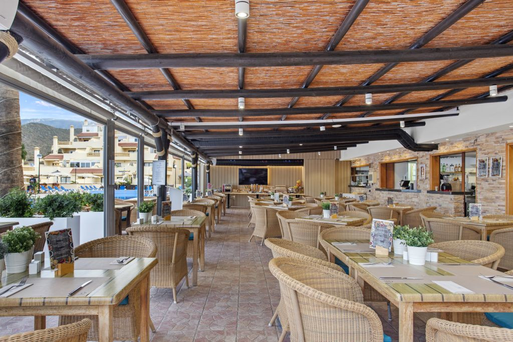 Salle à manger extérieure couverte à Tenerife avec tables et chaises en osier.