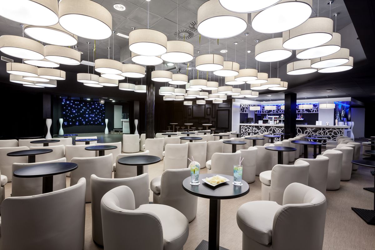 Salle moderne avec tables et fauteuils à Tenerife, lumières suspendues et bar en arrière-plan.