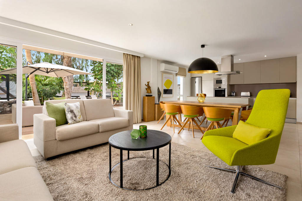 Salon moderne avec canapé, table ronde, chaises vertes et grande fenêtre à Tenerife.