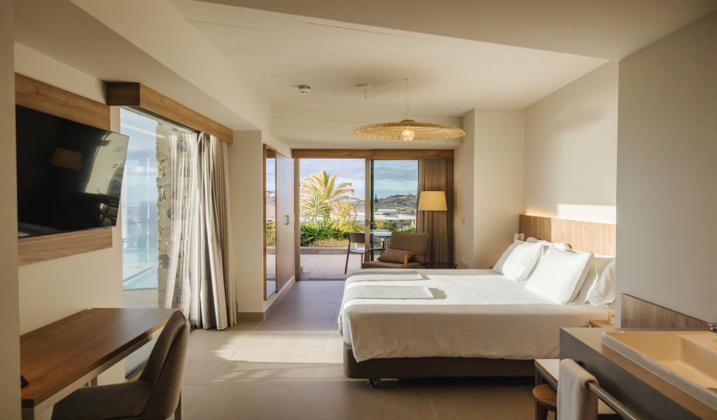 Chambre d'hôtel lumineuse avec lit double à Tenerife, vue sur terrasse et palmiers.