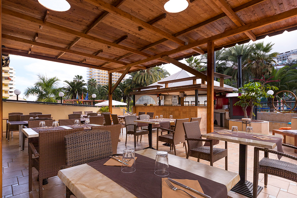 Terrasse de restaurant en plein air à Tenerife, avec tables et chaises en osier.