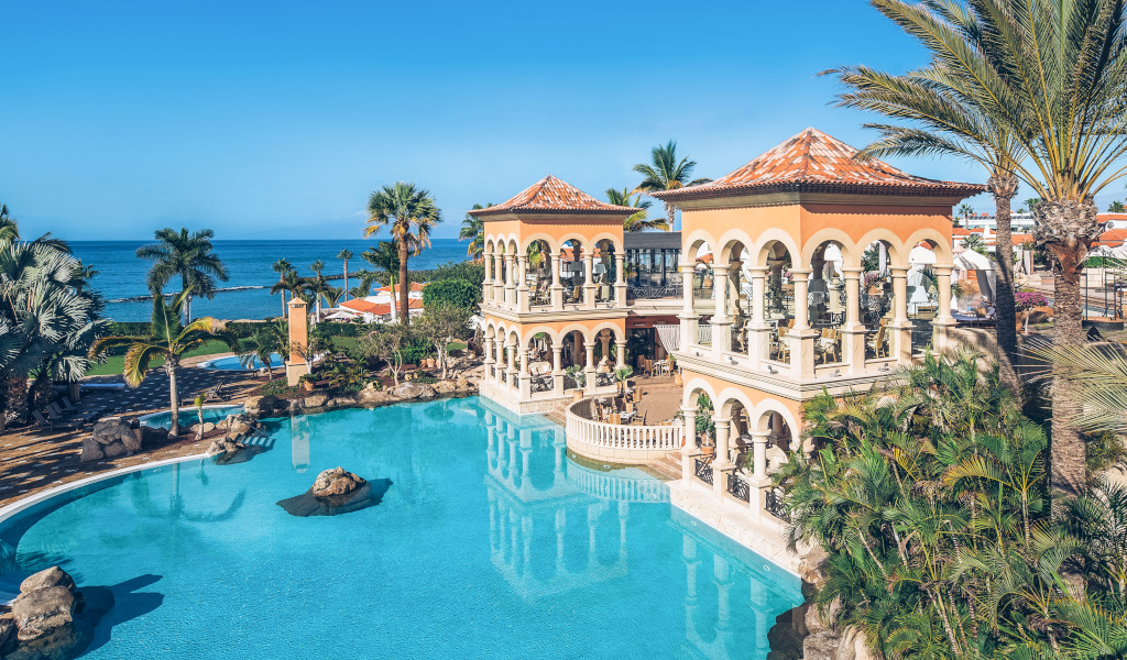 Bâtiment avec piscine entouré de palmiers à Tenerife, près de la mer.