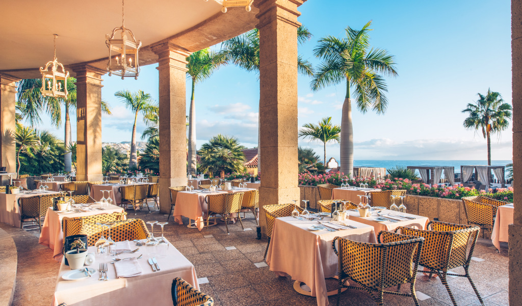Terrasse de restaurant avec tables dressées, palmiers et vue mer à Tenerife.