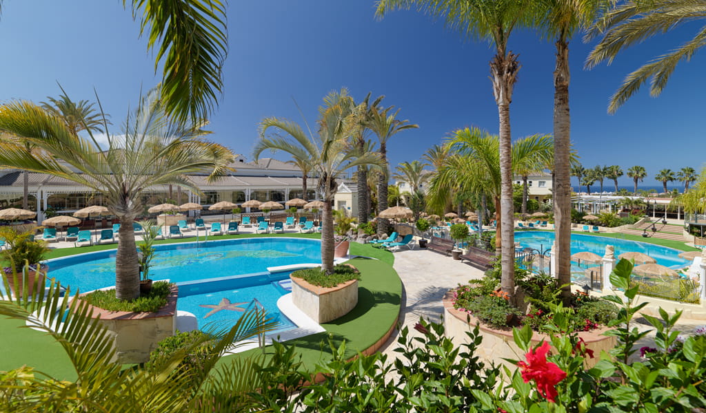 Piscine entourée de palmiers dans un complexe à Tenerife, avec ciel bleu et transats.