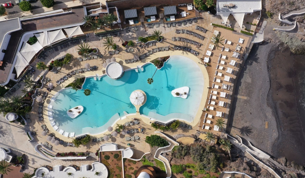 Piscine de complexe touristique à Tenerife, entourée de chaises longues et palmiers.