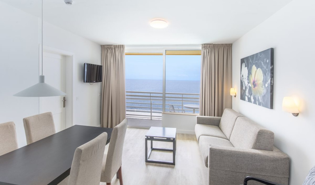 Salon avec vue sur l'océan à Tenerife, canapé, table, TV murale et tableau floral.