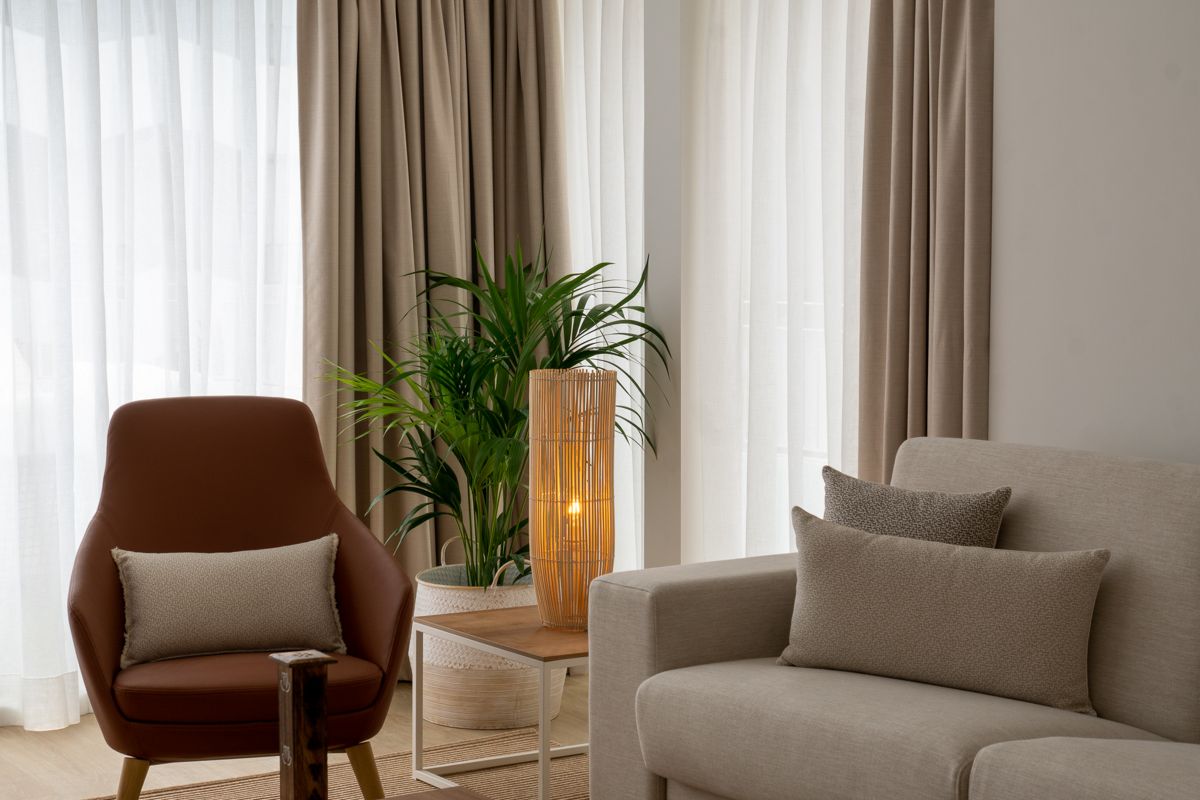 Fauteuil brun et canapé beige avec coussins, plante et lampe, Tenerife.