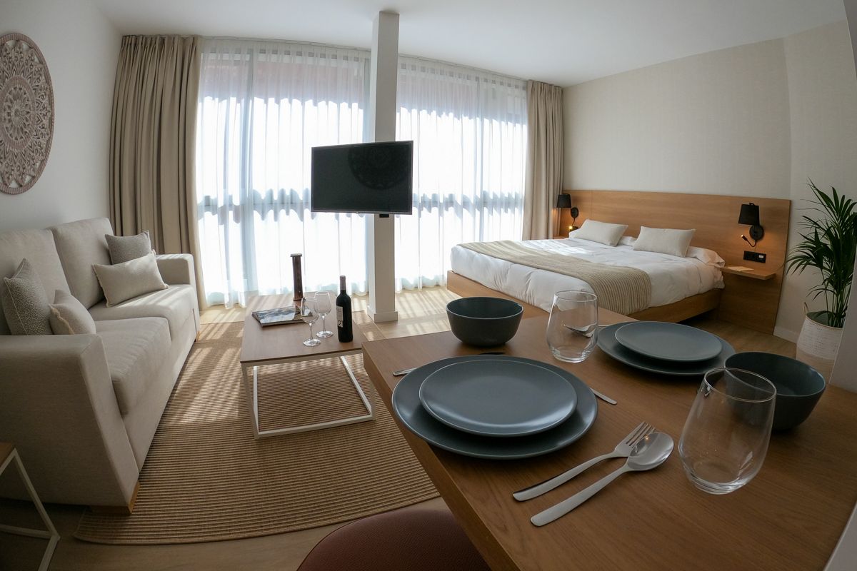 Chambre lumineuse à Tenerife avec lit, canapé, table dressée et grande fenêtre.