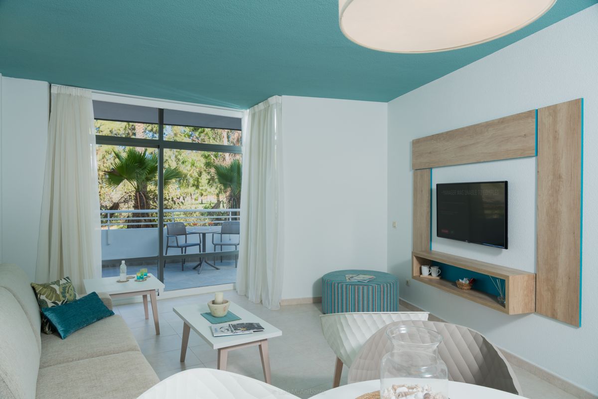 Salon lumineux avec canapé, tables basses, TV murale et balcon sur jardin à Tenerife.