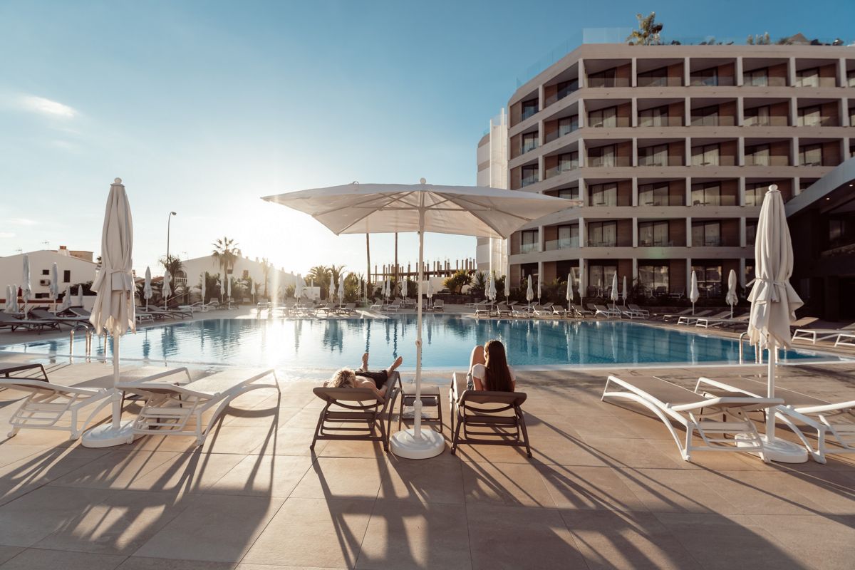 Transats au bord de la piscine d'un hôtel à Tenerife avec parasols et soleil couchant.