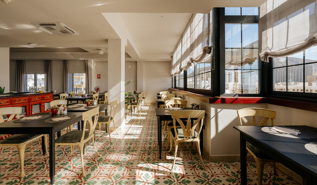 Salle de restaurant lumineuse à Los Cristianos, Tenerife, avec tables et fenêtres.