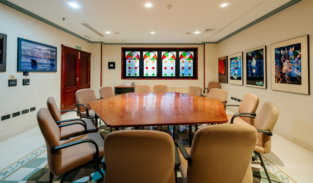 Salle de réunion avec grande table en bois à Tenerife, entourée de chaises et de vitraux.