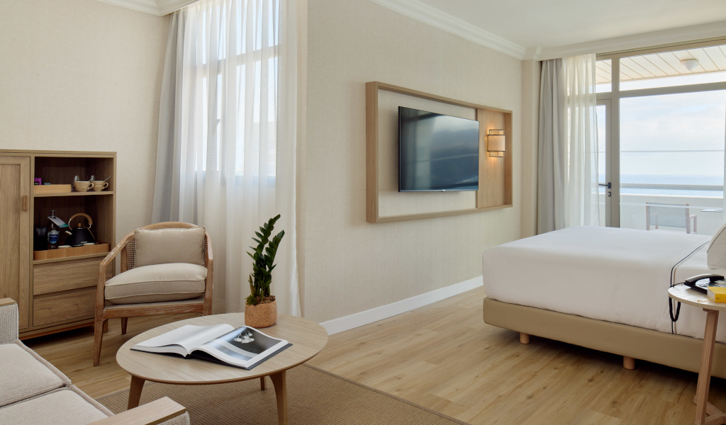 Chambre d'hôtel moderne avec lit, canapé, télé et vue sur la mer à Tenerife.