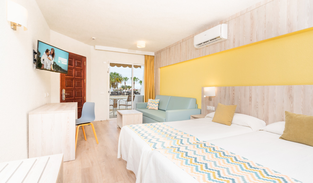 Chambre d'hôtel à Tenerife avec deux lits, canapé, TV et balcon.