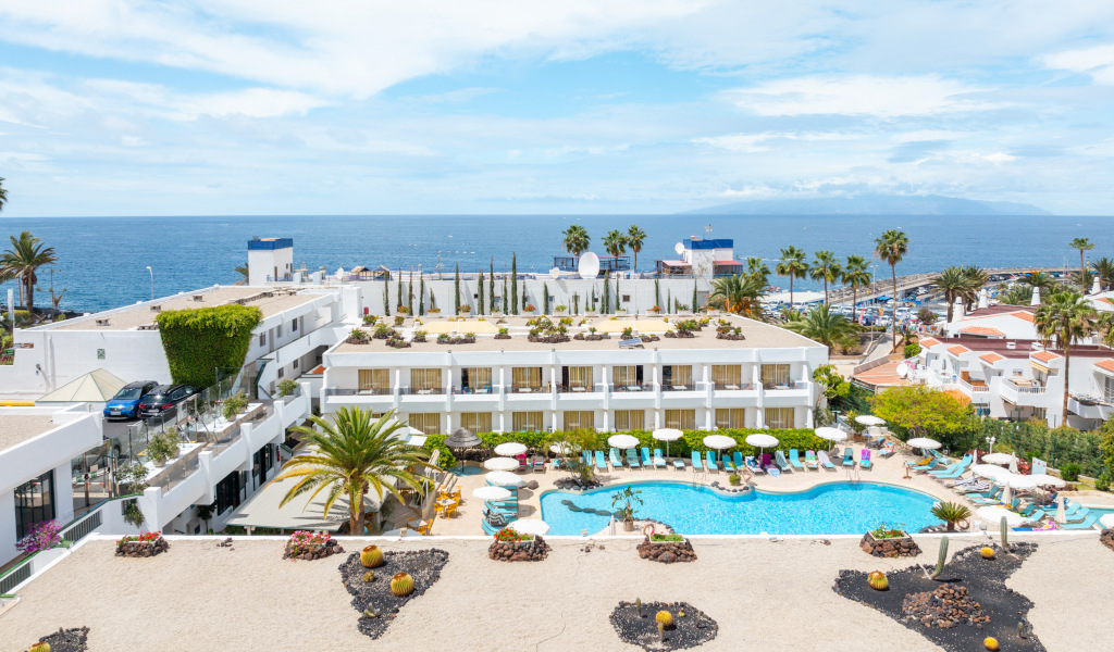 Complexe hôtelier avec piscine surplombant l'océan à Tenerife, entouré de palmiers.
