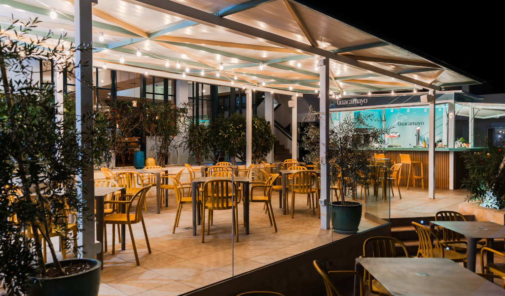 Terrasse éclairée d'un restaurant à Tenerife avec chaises et tables vides. Texte visible: Guacamayo.