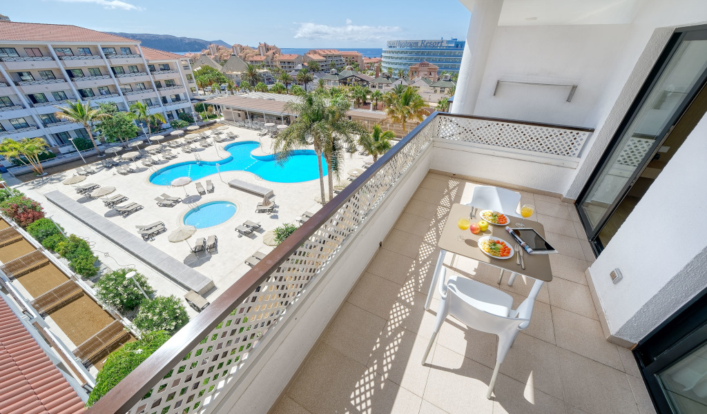 Balcon avec vue sur piscine et bâtiments à Tenerife, petit-déjeuner sur la table.