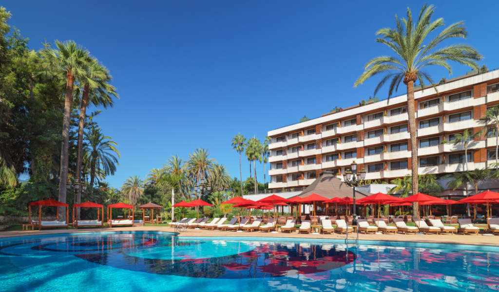 Piscine entourée de chaises longues et parasols rouges devant un hôtel à Tenerife.
