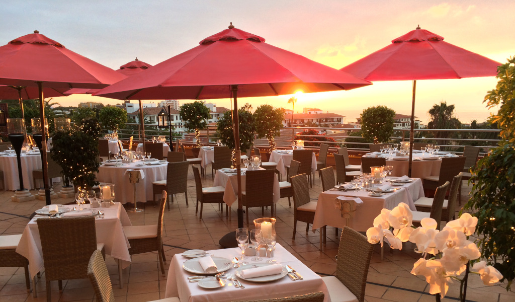 Terrasse de restaurant à Tenerife avec tables dressées sous parasols rouges.