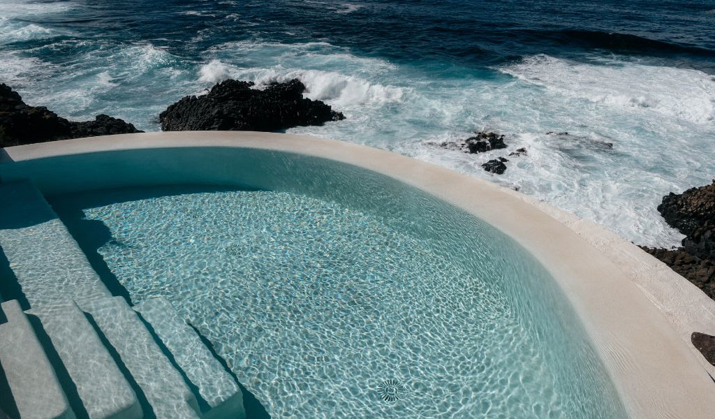 Piscine avec vue sur l'océan à Tenerife et rochers noirs en arrière-plan.