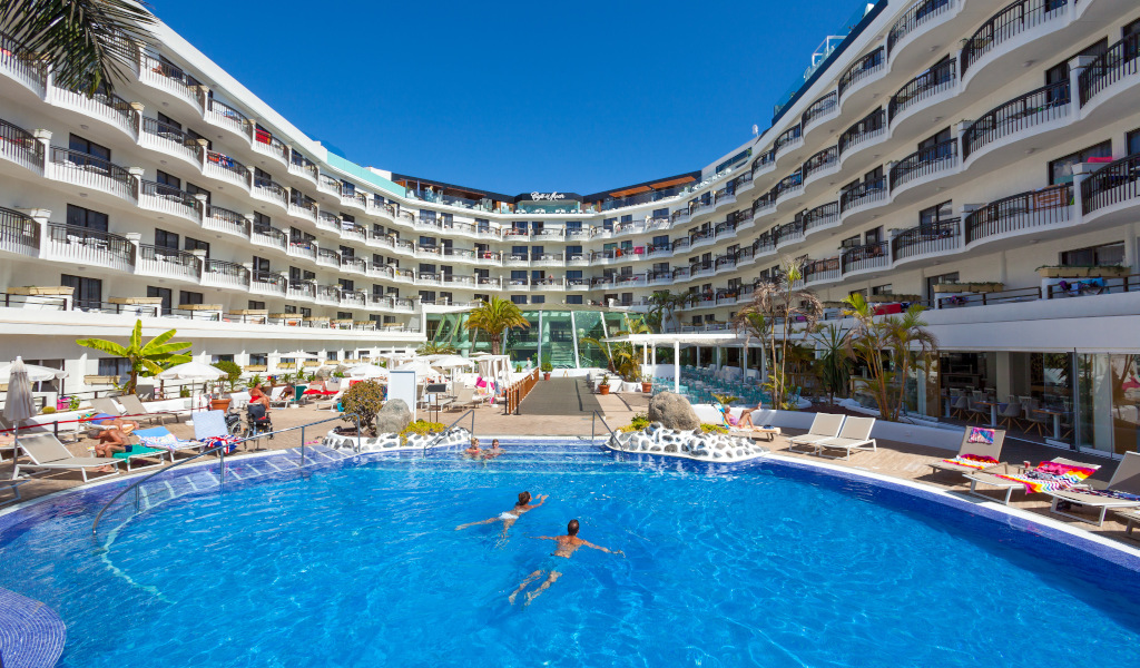 Piscine et bâtiment d'hôtel moderne à Tenerife, avec des personnes nageant.