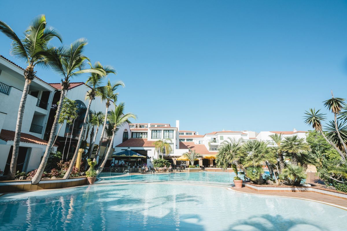 Piscine entourée de palmiers et bâtiments à Tenerife sous ciel bleu.