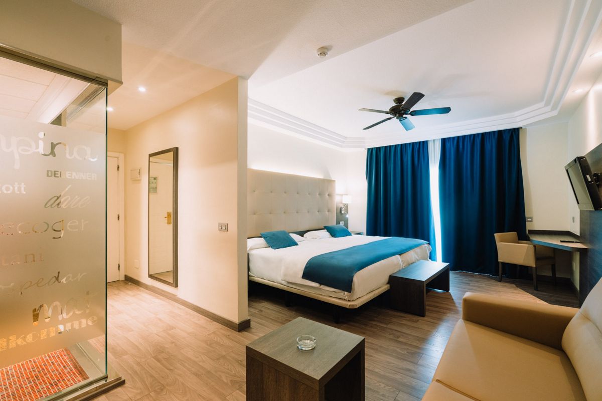 Chambre d'hôtel moderne à Tenerife avec grand lit, bureau et rideaux bleus.