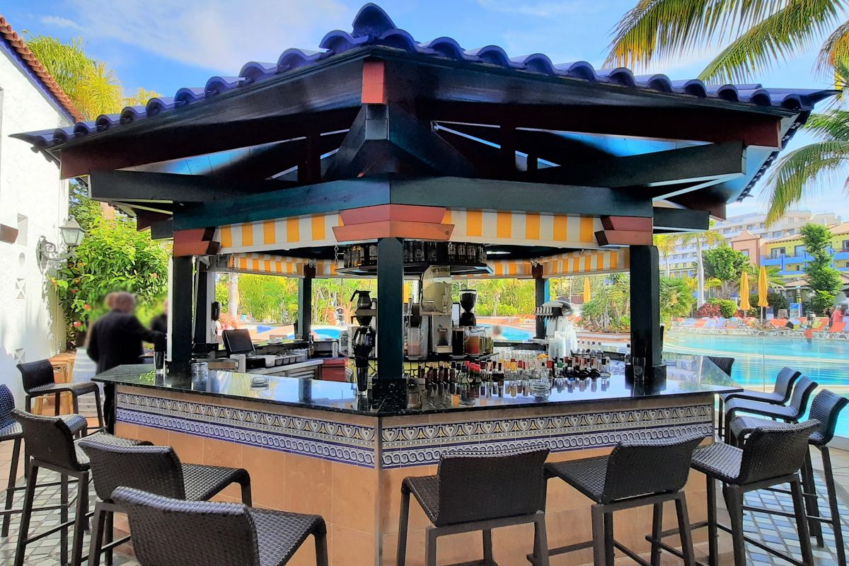 Bar extérieur près d'une piscine à Tenerife, tabourets autour, cocktails prêts.