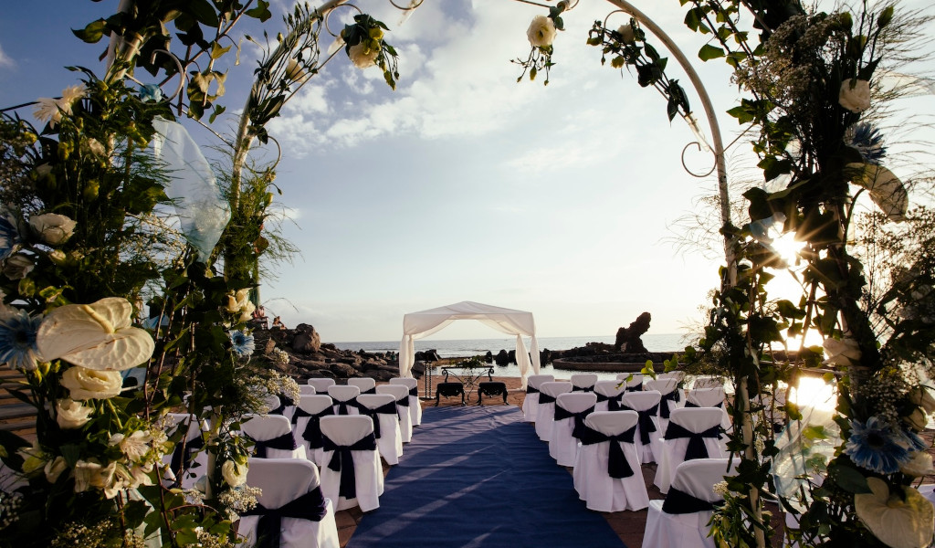 Chaises blanches et arche florale pour mariage en bord de mer à Tenerife.