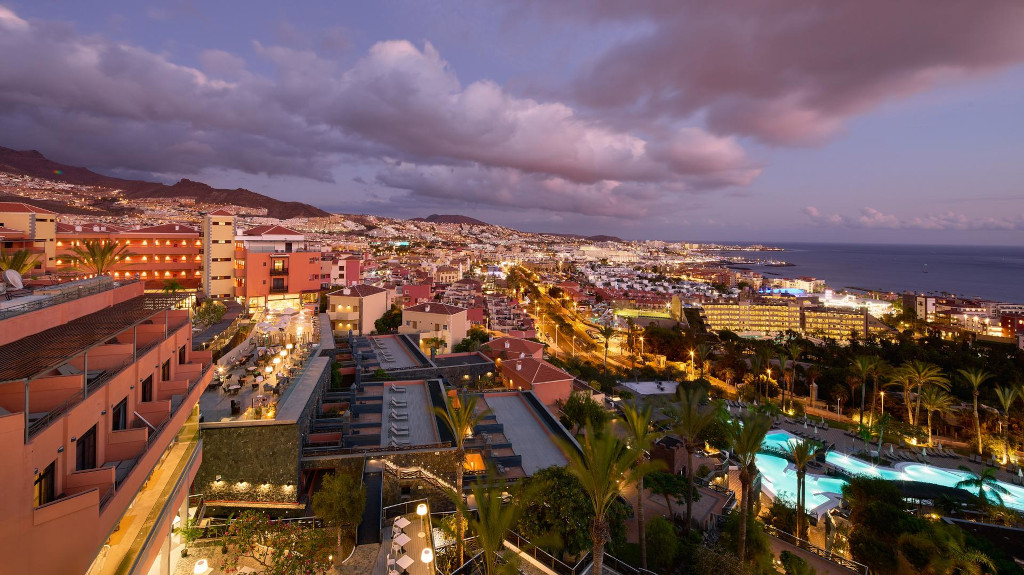 Vue nocturne de Los Cristianos, Tenerife, avec bâtiments illuminés et piscine.