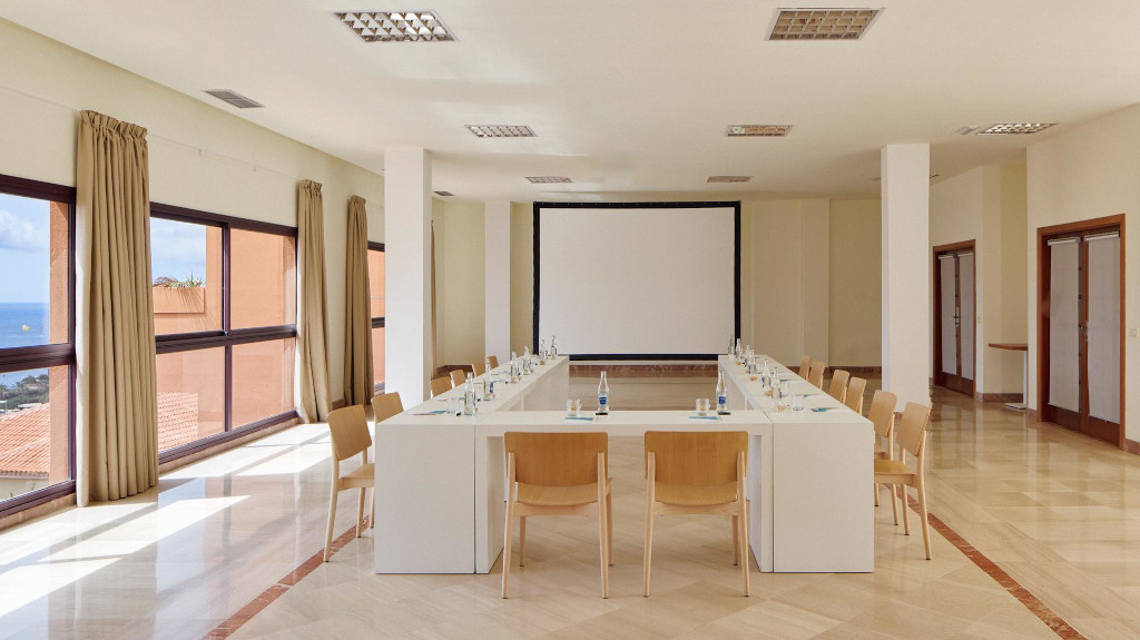 Salle de conférence avec vue sur l'océan à Tenerife, tables en U et écran blanc.