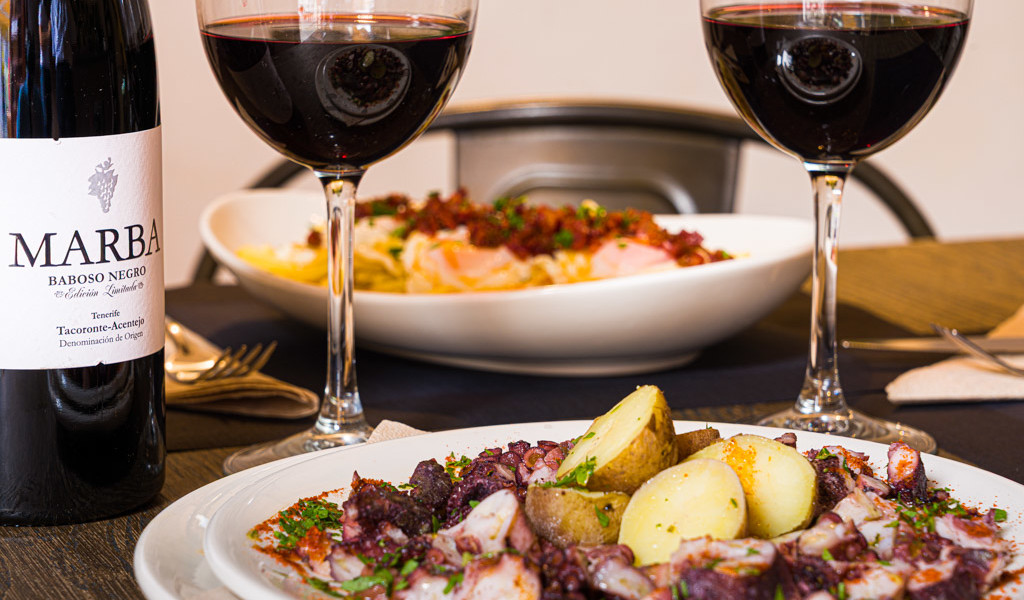 Pulpo avec pommes de terre, deux verres de vin rouge, bouteille Marba Baboso Negro. Tacoronte-Acentejo.